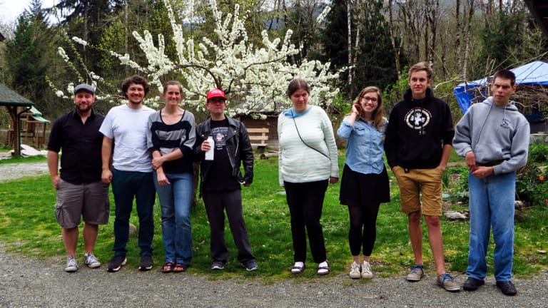 A group of people ranging from their teens to middle-aged pose together in front of a small tree with white flowers.