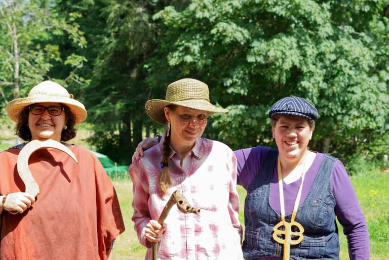 Three women are dressed in light costumes for a play. They are wearing hats and have some tools as props.