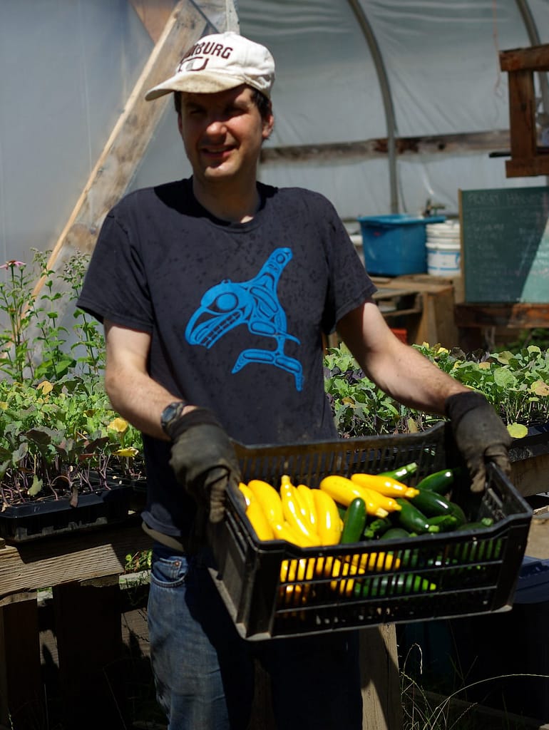 A young man holds a basket full of yellow and green zucchini.