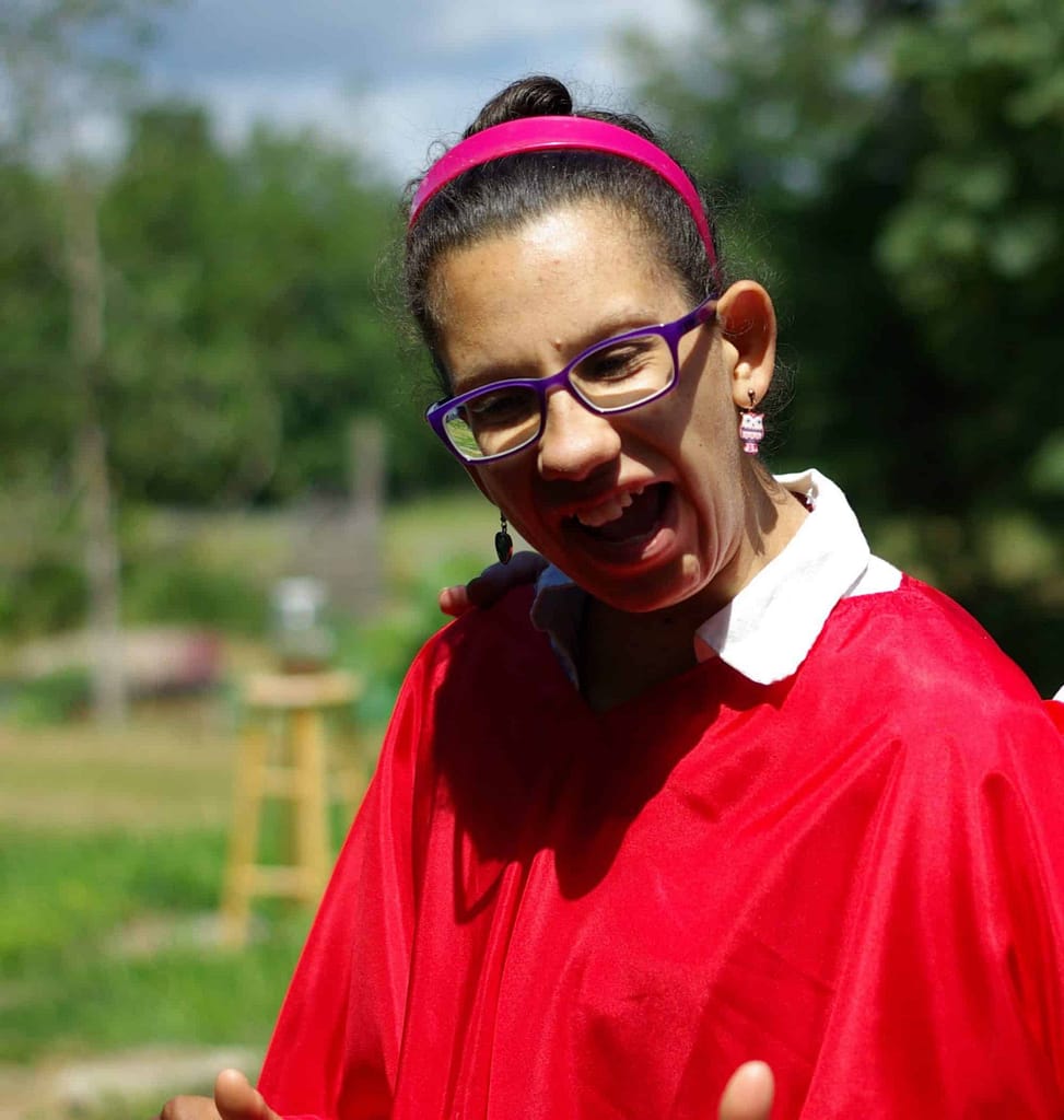 A young woman laughs. She is wearing a bright red shirt and glasses.